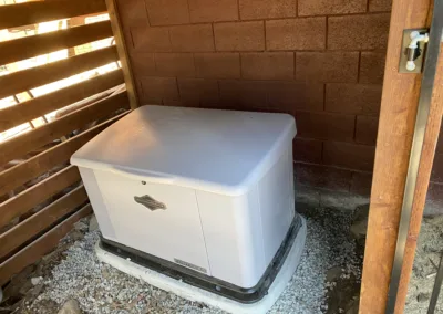 Standby generator installed next to a brick wall in a structure with wooden slats.